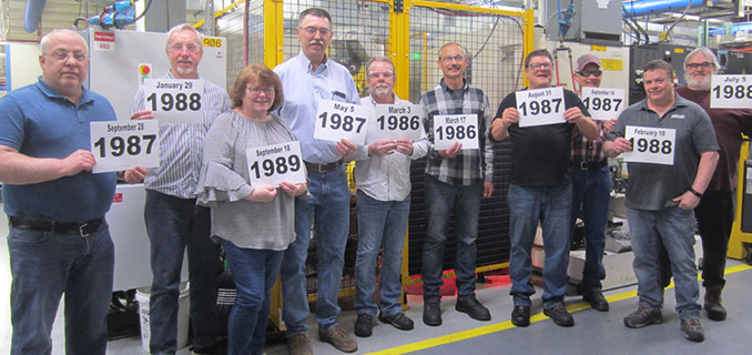 A group of Horton employees in the Britton plant holding up signs with the year they were hired.